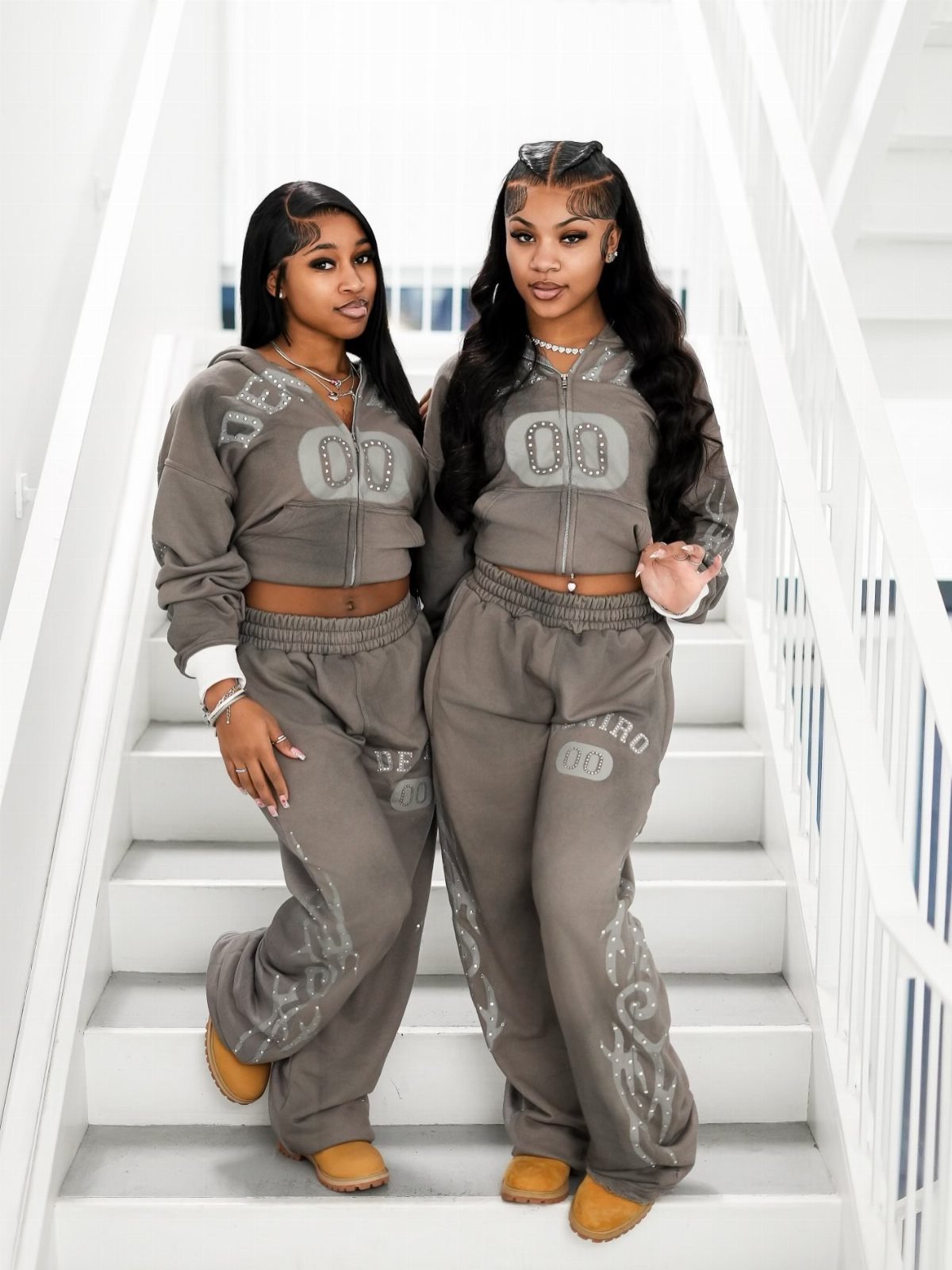 12 Super Bowl Outfits From Sporty to Sequined for Game Day 6 Two women wearing matching grey cropped hoodies and wide-leg sweatpants on white stairs.
