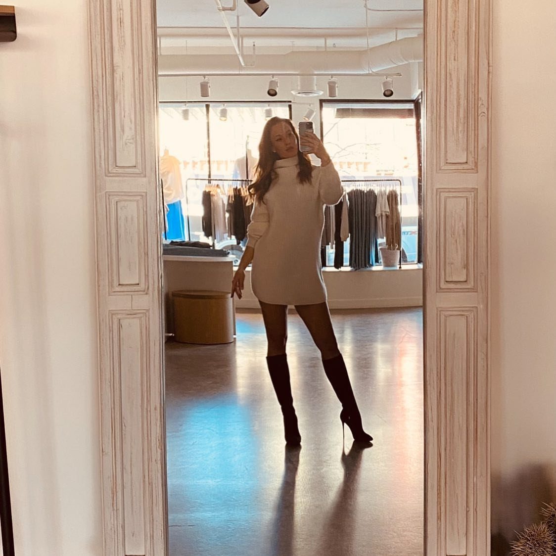 12 Super Bowl Outfits From Sporty to Sequined for Game Day 3 Woman in a white sweater dress and tall black boots posing in a mirror.