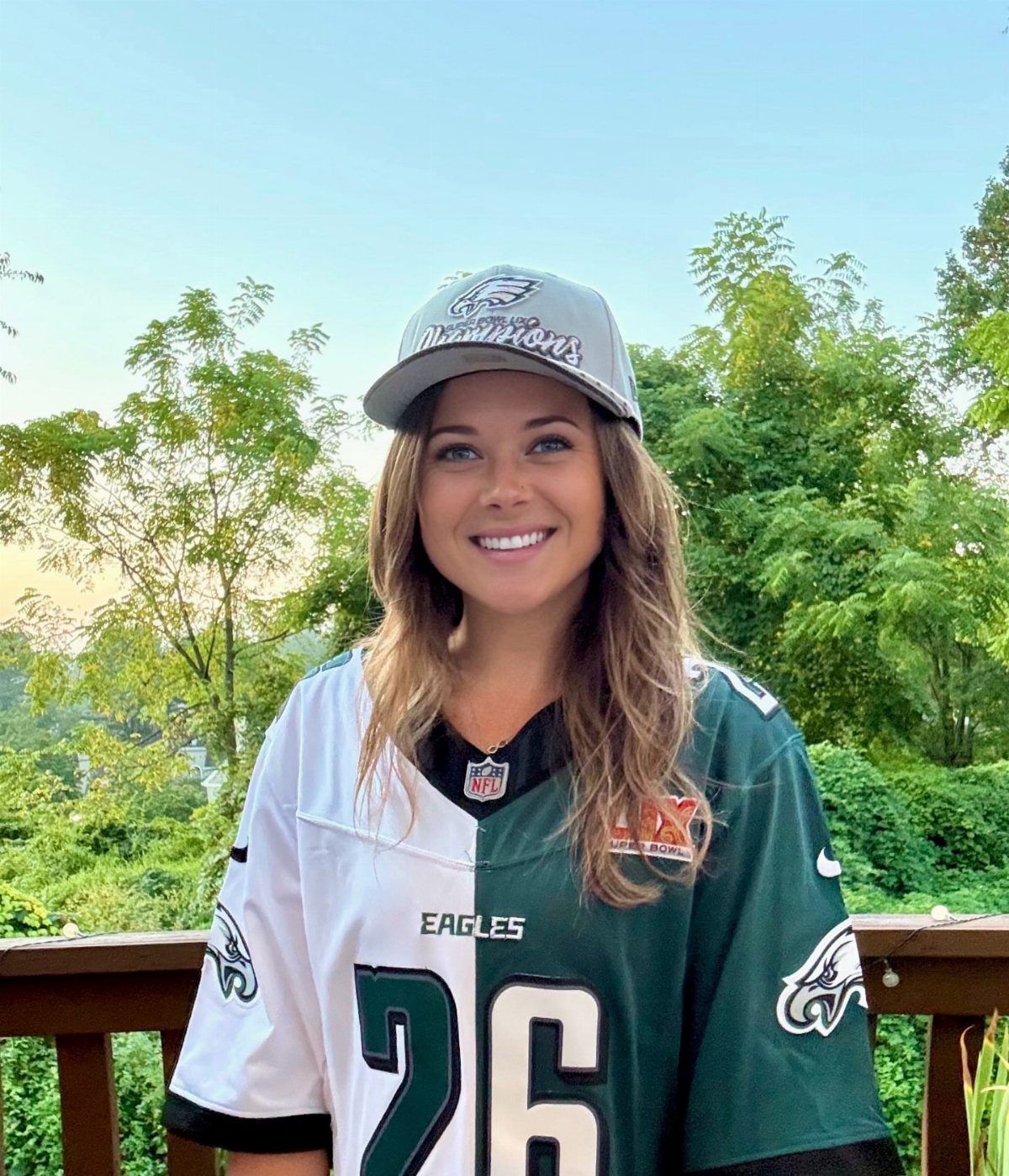 12 Super Bowl Outfits From Sporty to Sequined for Game Day 7 Woman wearing a Philadelphia Eagles jersey and matching baseball cap smiling outdoors.
