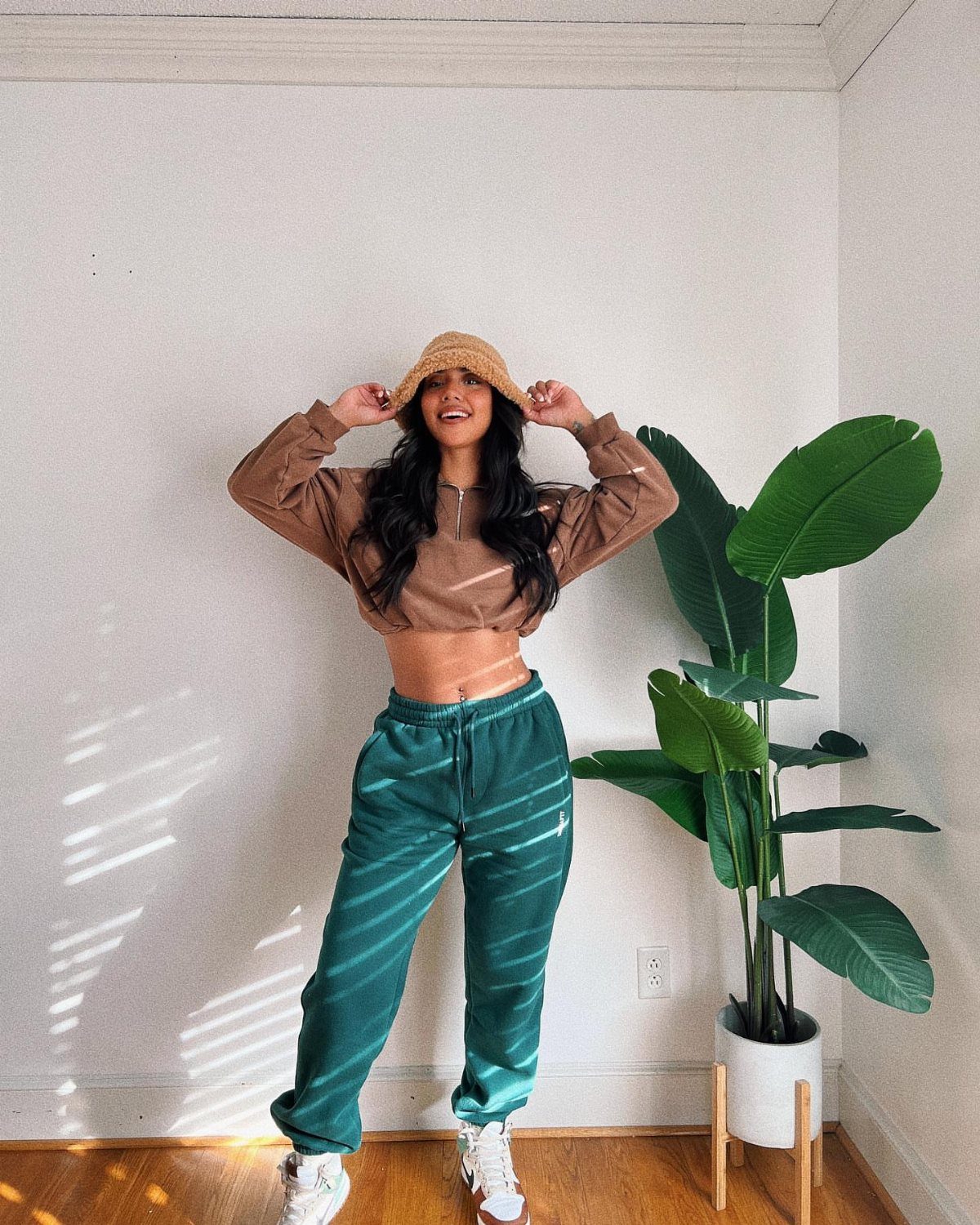 12 Super Bowl Outfits From Sporty to Sequined for Game Day 1 Woman wearing a brown cropped top, green track pants, and a bucket hat.