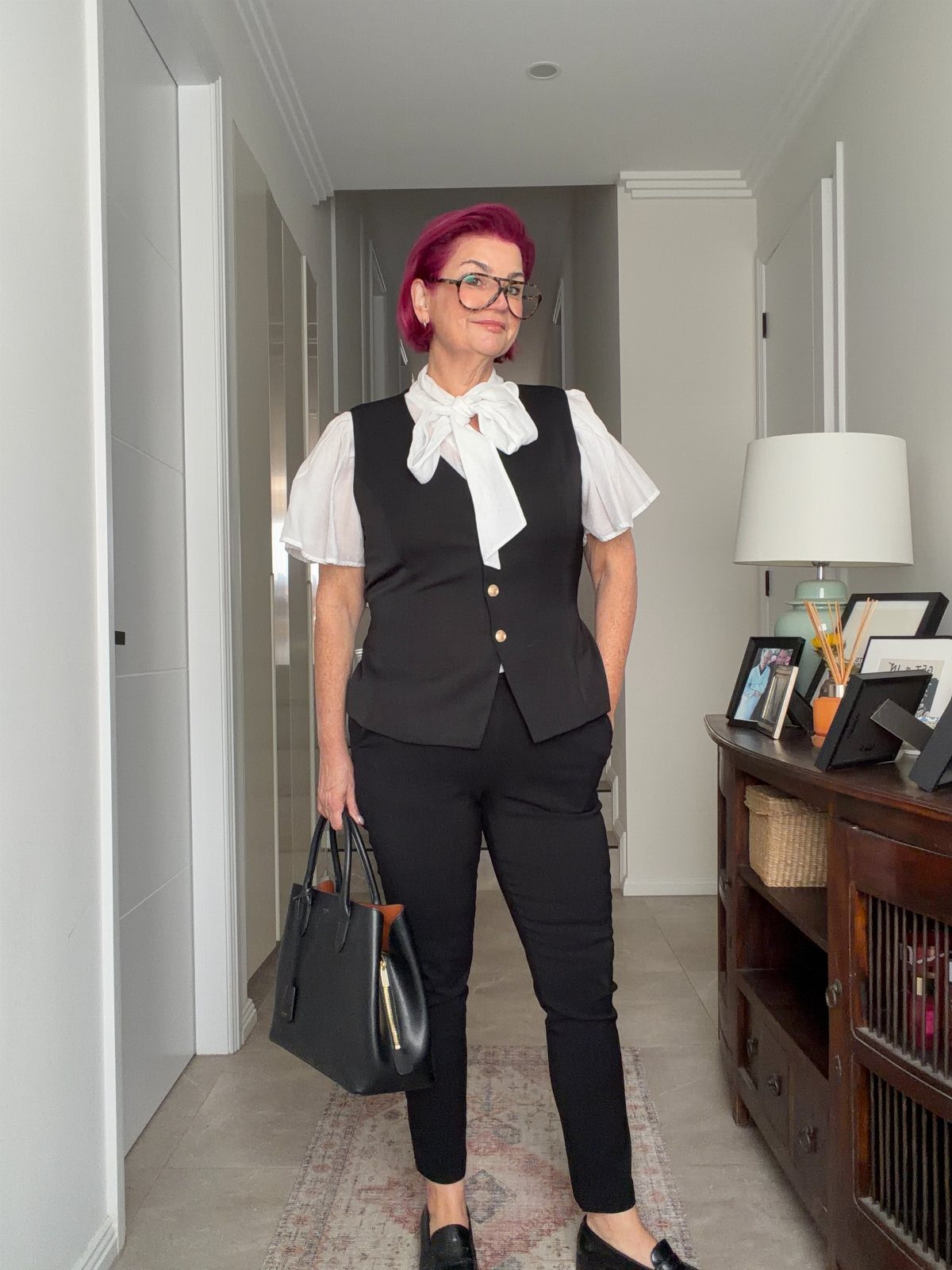 Tea Party Outfits for Adults: 10 Ideas from Garden to High Tea 4 Woman with pink hair wearing a black vest, white bow blouse, and black trousers.