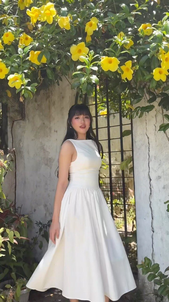 Tea Party Outfits for Adults: 10 Ideas from Garden to High Tea 1 Woman in a white vintage-style tea length dress standing under yellow flowering vines.
