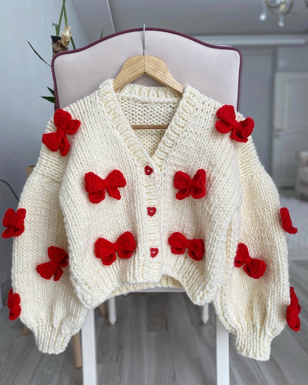 Twice This Is For Outfits: 6 Concert-Ready Looks to Recreate 6 Cream knit cardigan with red crochet bows hanging on a wooden hanger.