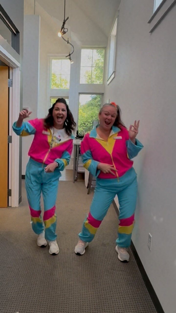 7 Wacky Wednesday Outfits for School, Work & Beyond 6 Two women wearing bright neon pink and blue tracksuits posing in a hallway.