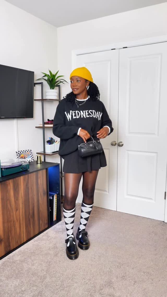 7 Wacky Wednesday Outfits for School, Work & Beyond 7 Person wearing a Wednesday sweatshirt, yellow beanie, and checkered socks in a room.