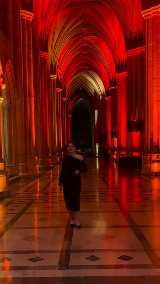 Washington DC Outfits: 11 Stylish Ideas for Your Trip 4 Woman in a black off-the-shoulder evening dress standing in a red-lit vaulted hall.