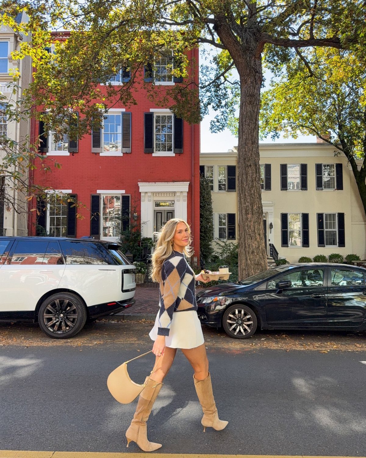 Washington DC Outfits: 11 Stylish Ideas for Your Trip 9 Blonde woman in a patterned sweater and white skirt walking on a city street.
