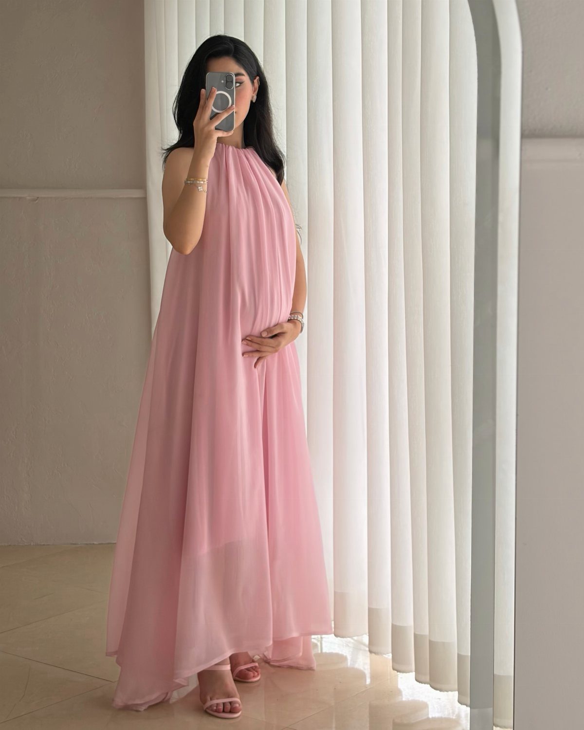 Women's Mother of the Bride Dresses in 8 Classic Styles 6 Woman in a long, sleeveless light pink chiffon dress standing before white curtains.