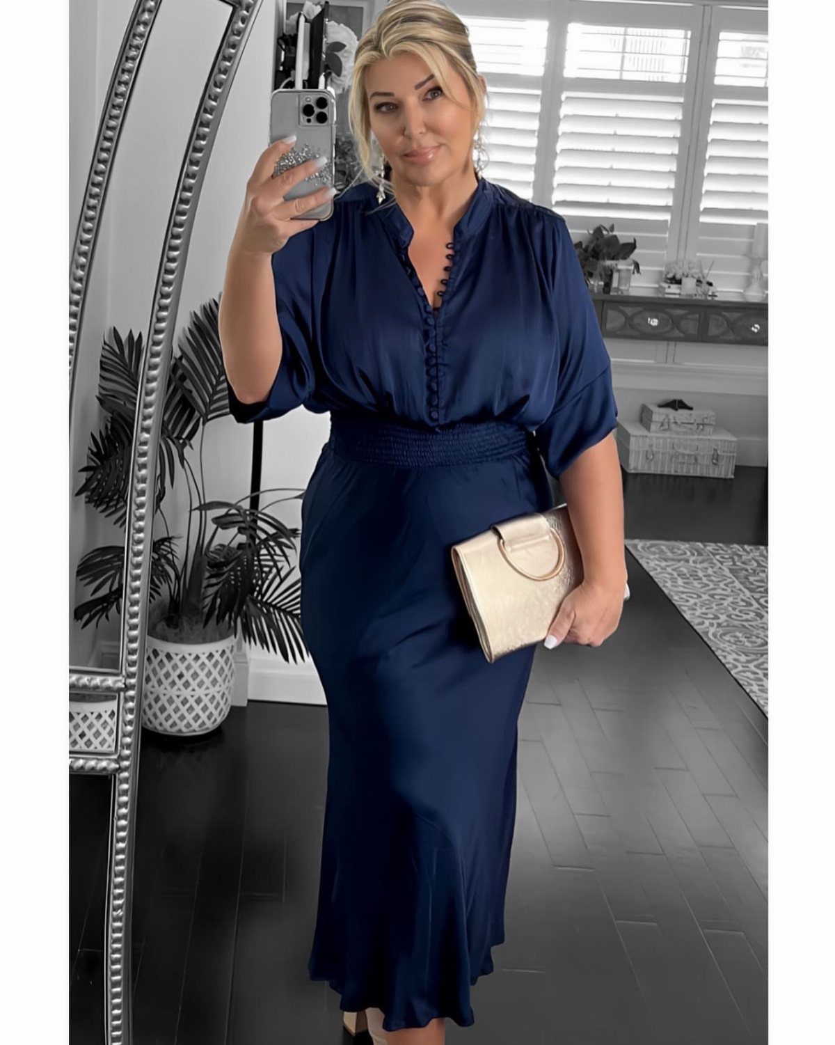 Women's Mother of the Bride Dresses in 8 Classic Styles 4 Woman in a navy blue satin midi-length dress holding a gold clutch bag.