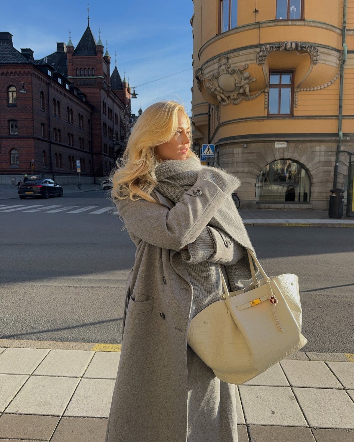 Women's Scarf Coat: 12 Ideas to Try This Season 5 Blonde woman wearing a long grey wool scarf coat and carrying a cream handbag.
