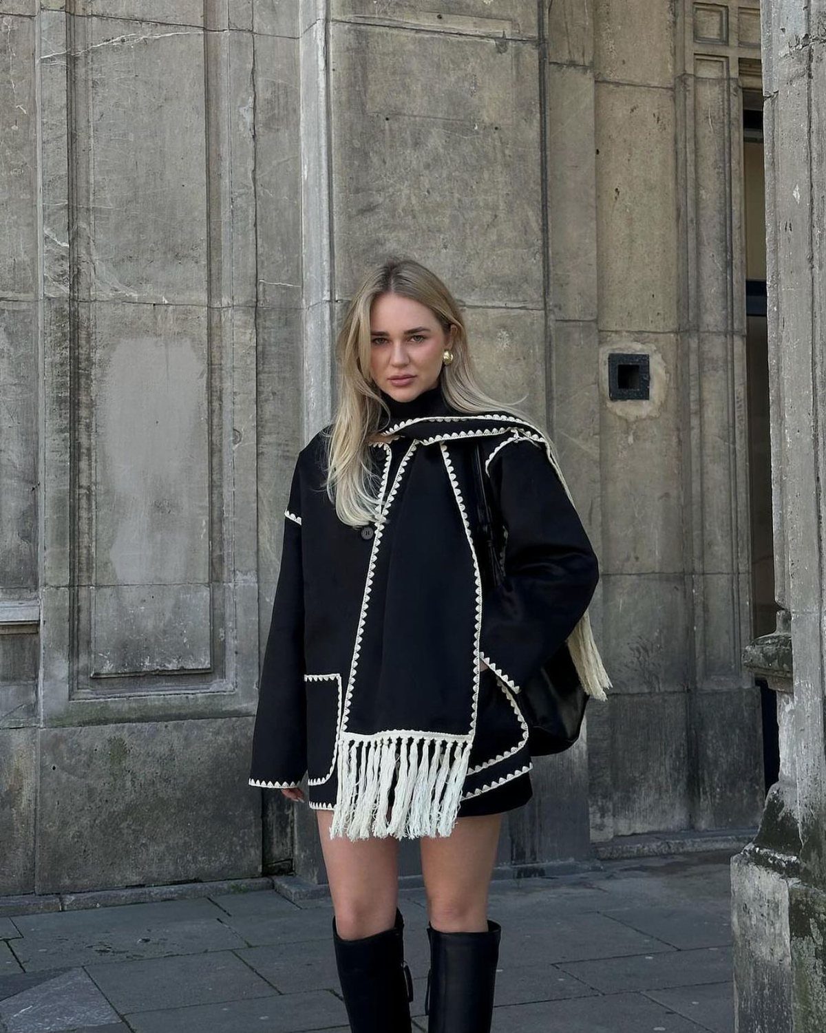Women's Scarf Coat: 12 Ideas to Try This Season 3 Woman wearing an oversized black wool-blend scarf jacket with white fringe and stitching.