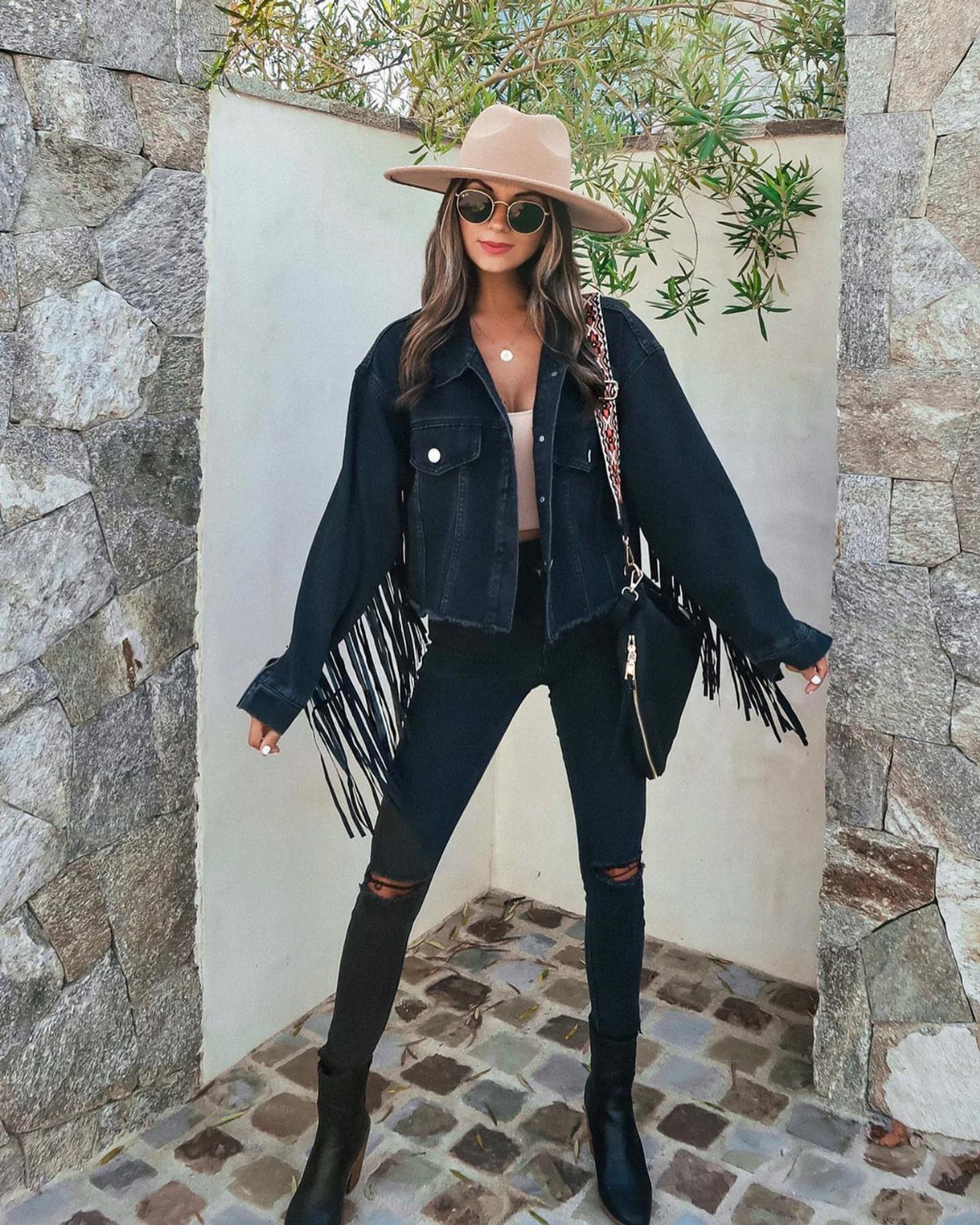 Women's Wild West Outfit Ideas: 9 Styles That Deliver 1 Woman wearing a dark denim jacket with long fringe and a tan cowboy hat.