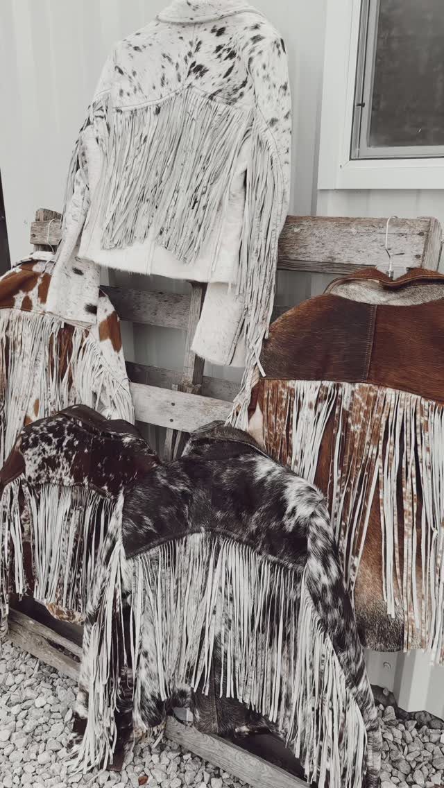 Women's Wild West Outfit Ideas: 9 Styles That Deliver 3 Fringed leather jackets in various colors and patterns draped over a wooden pallet.